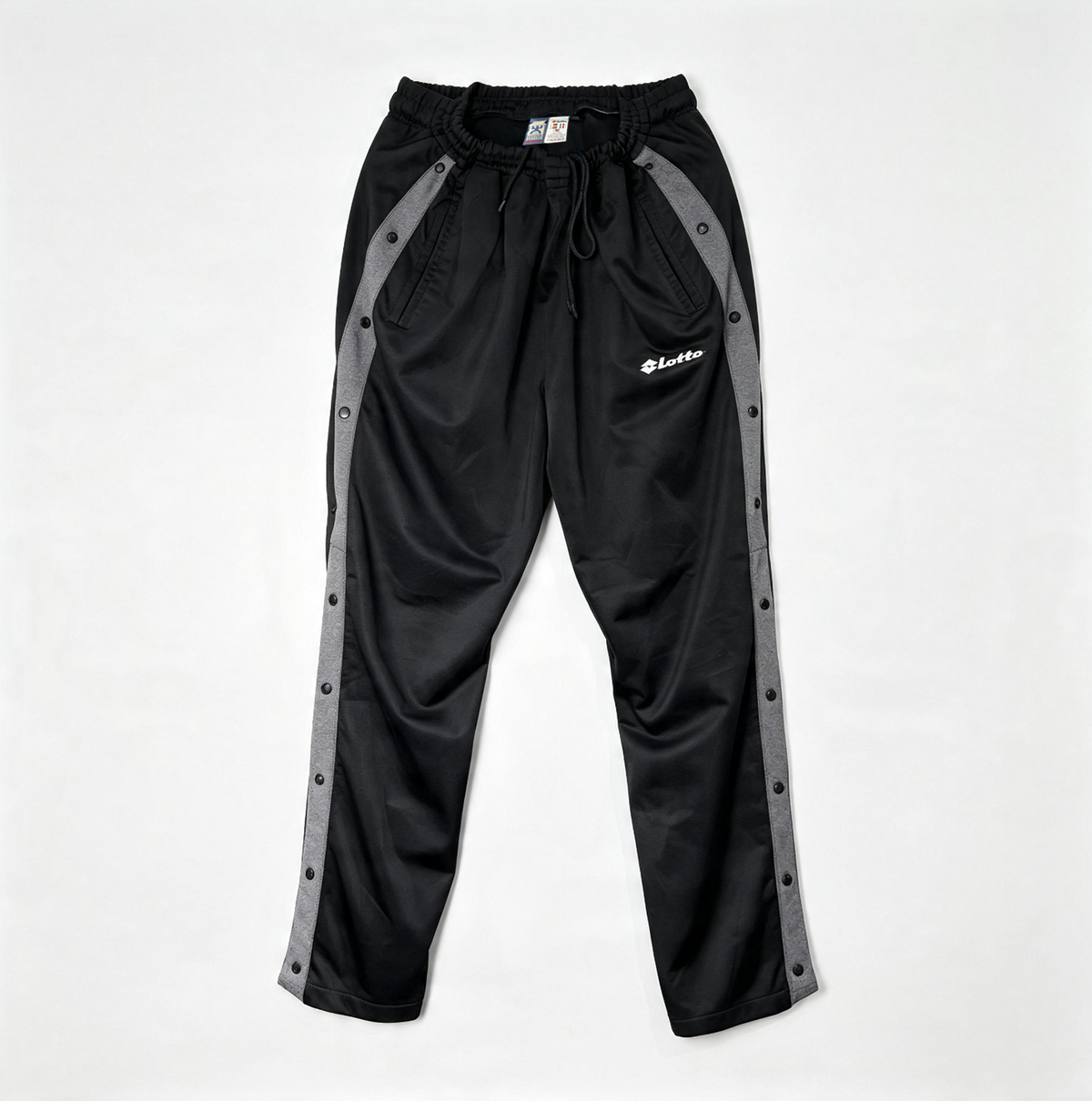 Black athletic pants with gray side panels and metal snap buttons, featuring a white 'Lululemon' logo on the left thigh, laid flat on a light gray background.