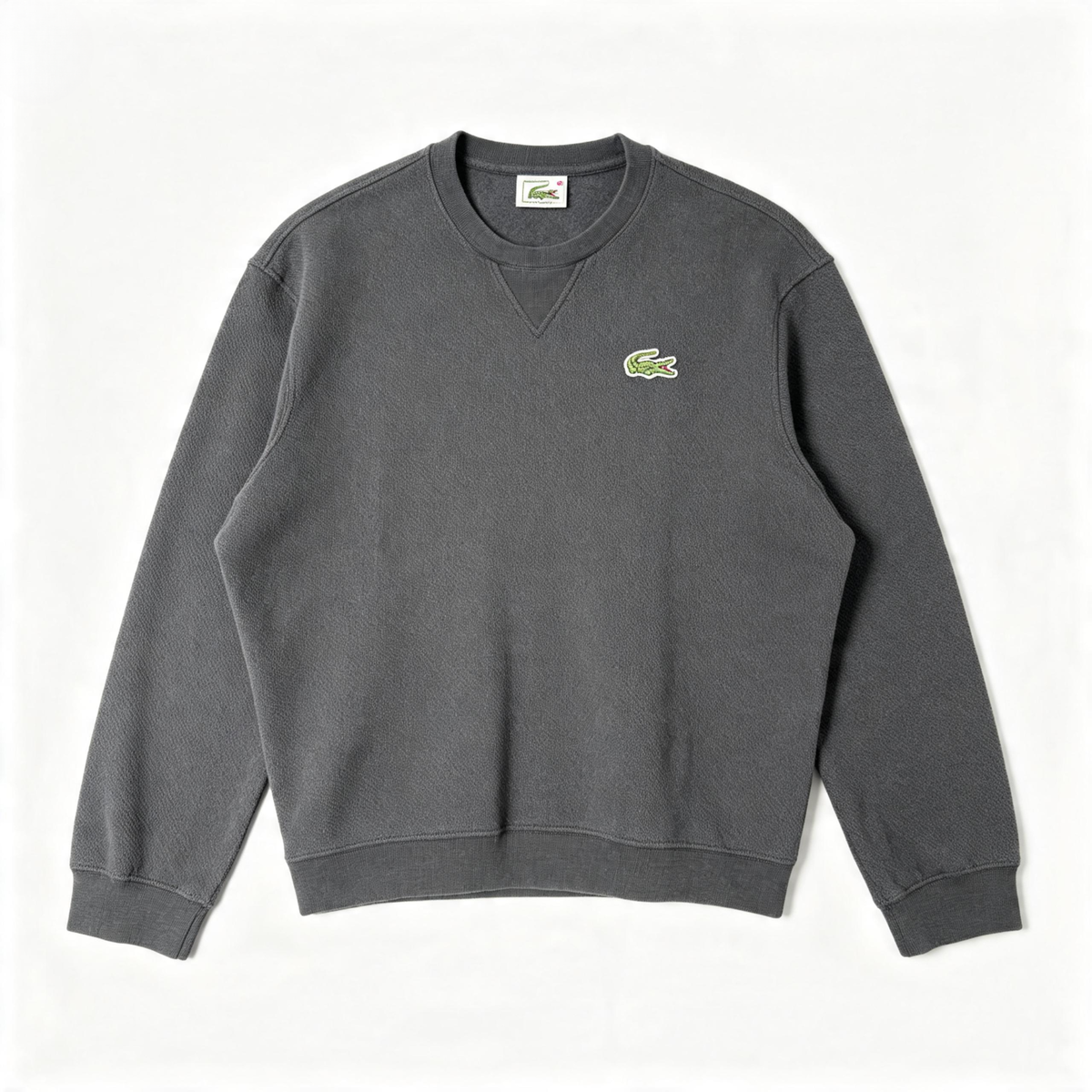 A dark gray crewneck sweatshirt featuring the iconic green and yellow Lacoste crocodile logo embroidered on the left chest, laid flat against a clean white background.