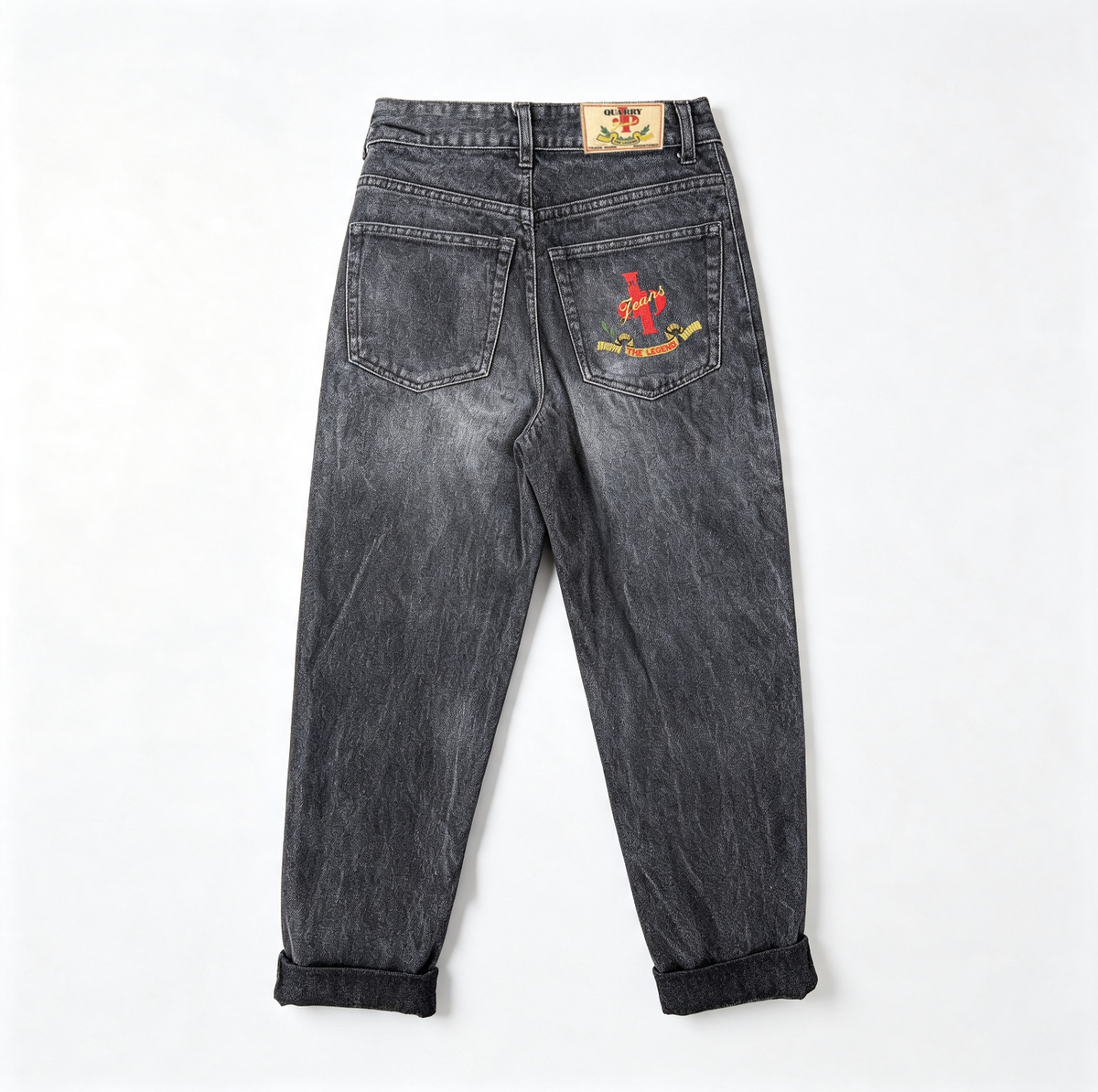 Back view of washed black denim jeans with rolled cuffs, featuring a red anchor graphic and text on the right back pocket and a small brand patch on the waistband.