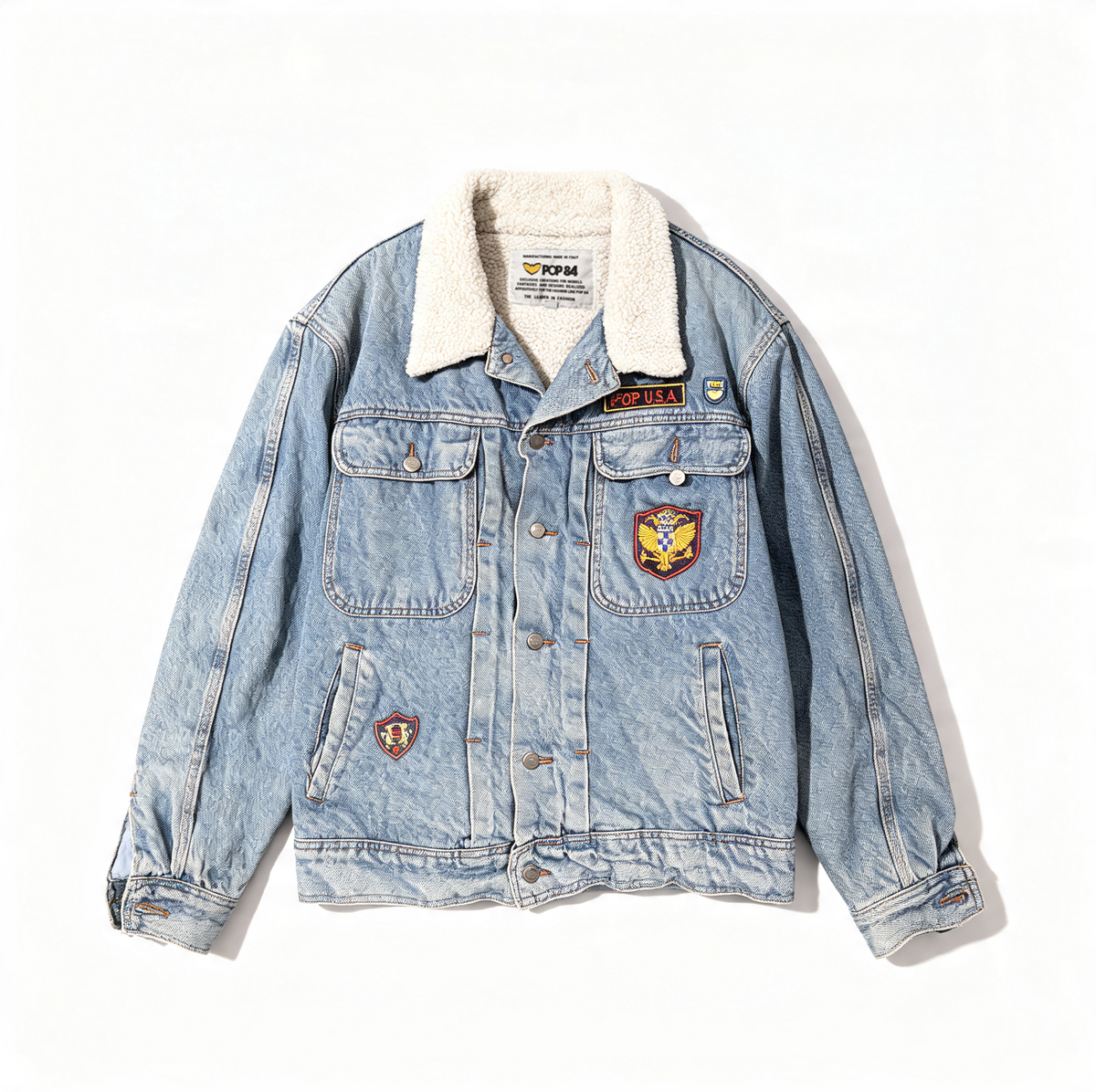 A light blue denim jacket with a white sherpa fleece collar, featuring multiple embroidered patches on the chest and pockets, photographed flat against a white background.