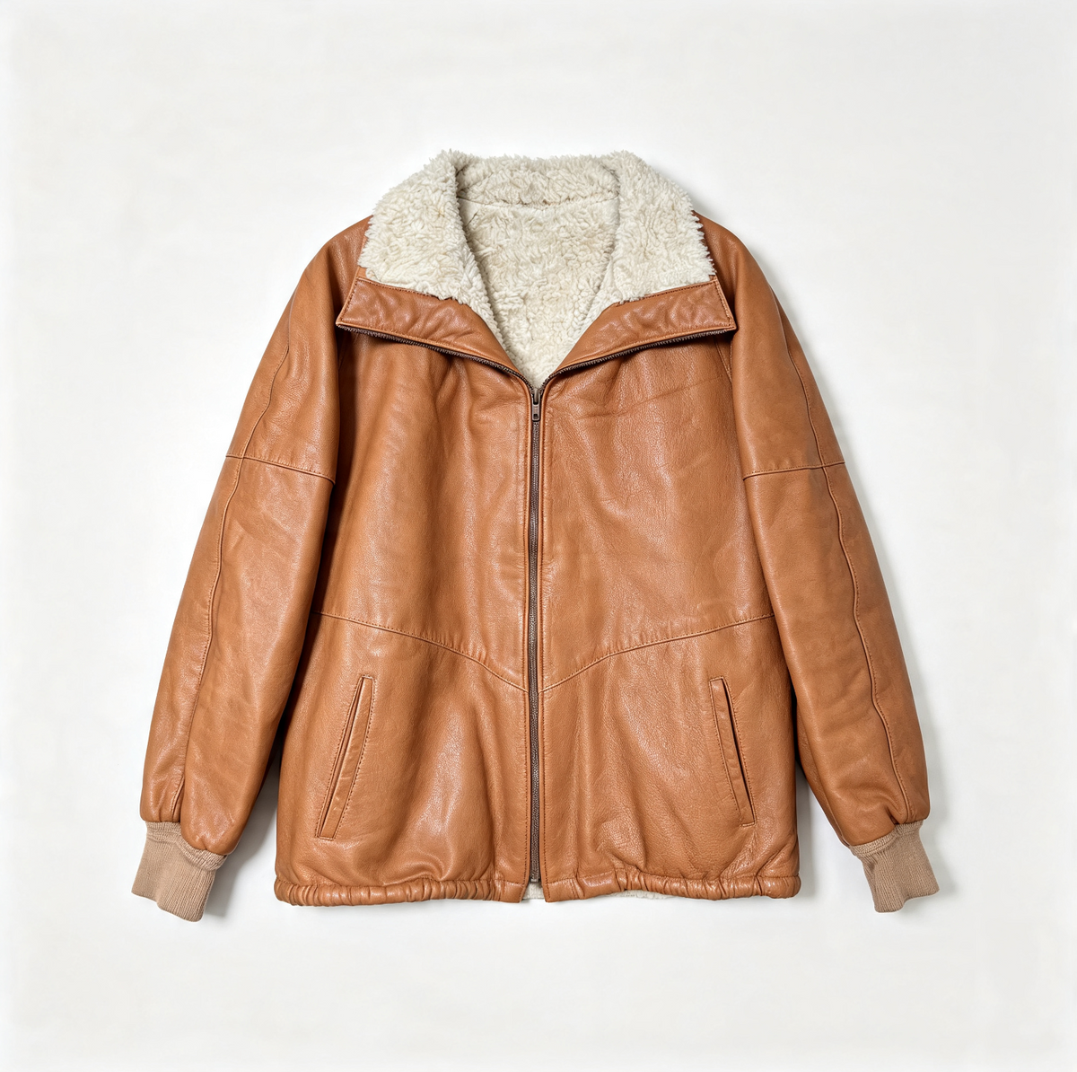 A tan leather jacket with a cream sherpa lining on the collar and cuffs, displayed flat against a light off-white background.