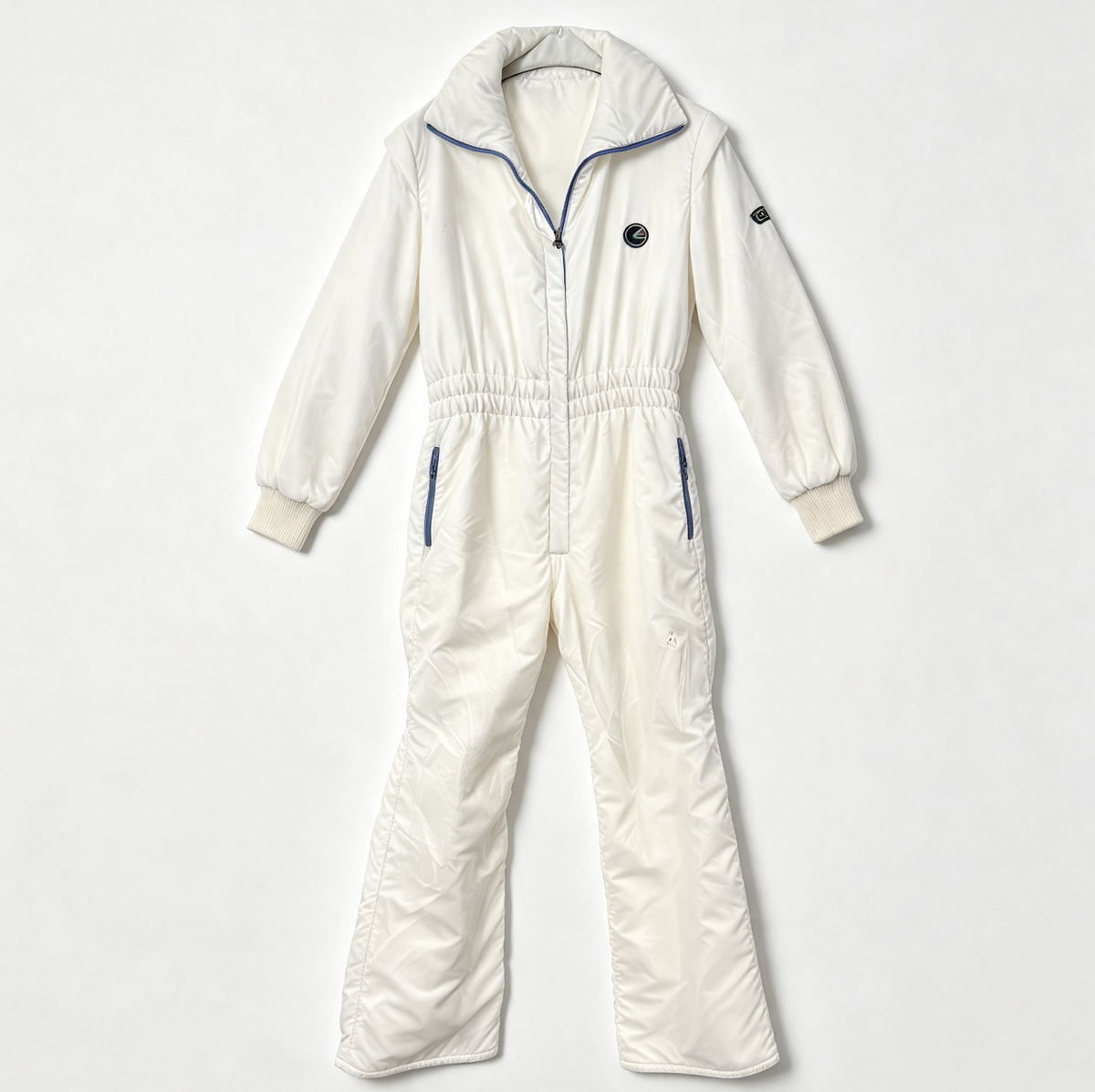An off-white puffer jumpsuit with blue piping accents, a front zipper, and elastic waistband, laid flat on a light gray background.