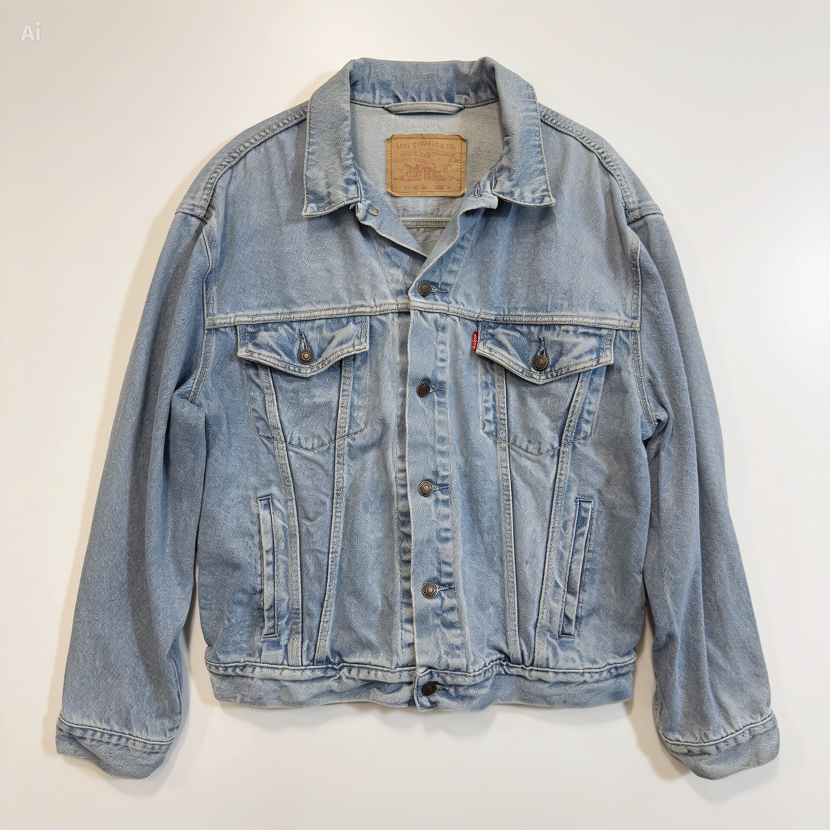 A light blue denim Levis's trucker jacket laid flat against a plain white background, featuring classic button-front closure, chest flap pockets, and signature red tab on the right chest.
