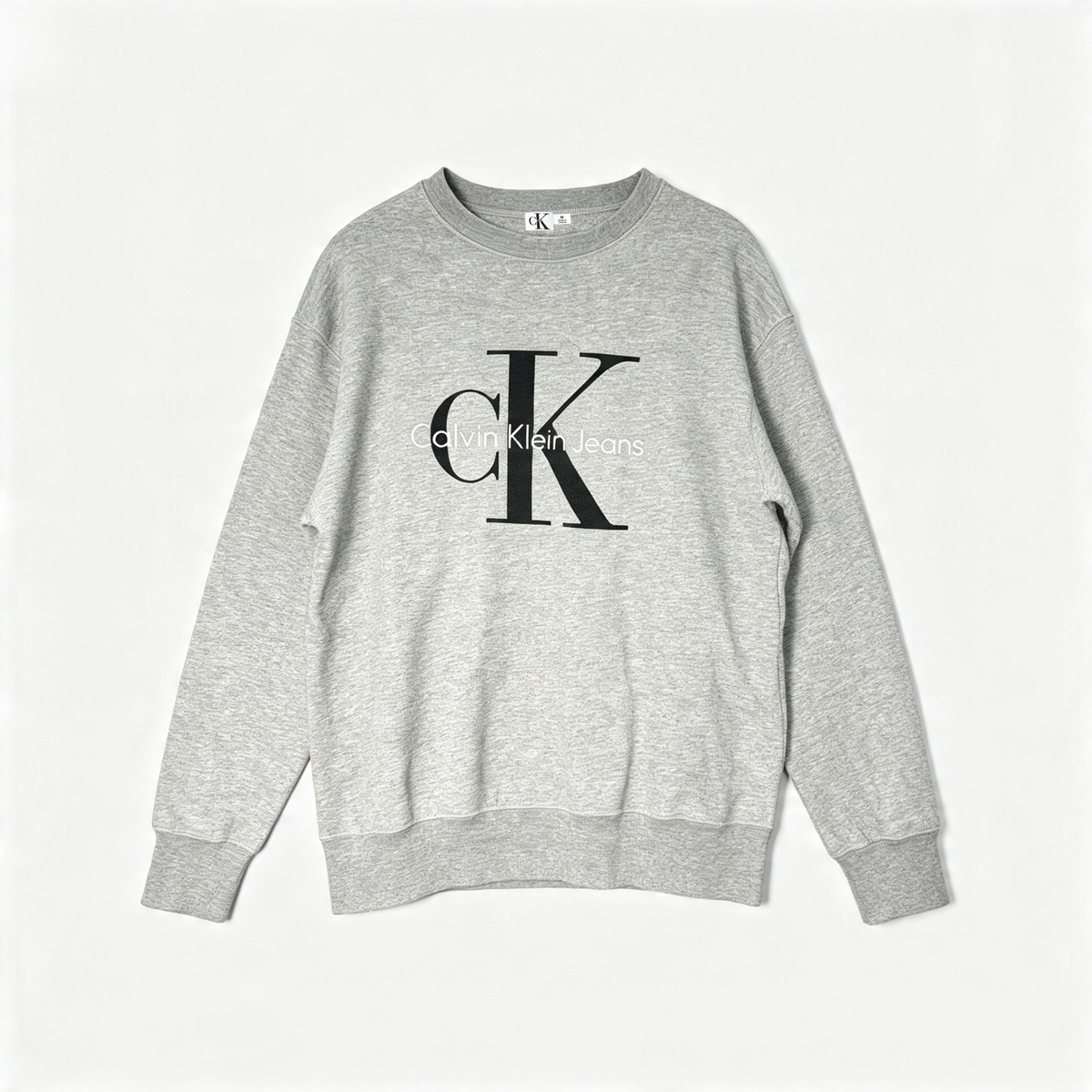 A light gray heather crewneck sweatshirt featuring a large black Calvin Klein Jeans 'ck' logo printed on the chest, displayed flat against a light gray background.