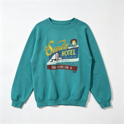 A teal crewneck sweatshirt featuring a vintage-style graphic print of 'The Sands Hotel' on the front, displayed flat against a clean white background.