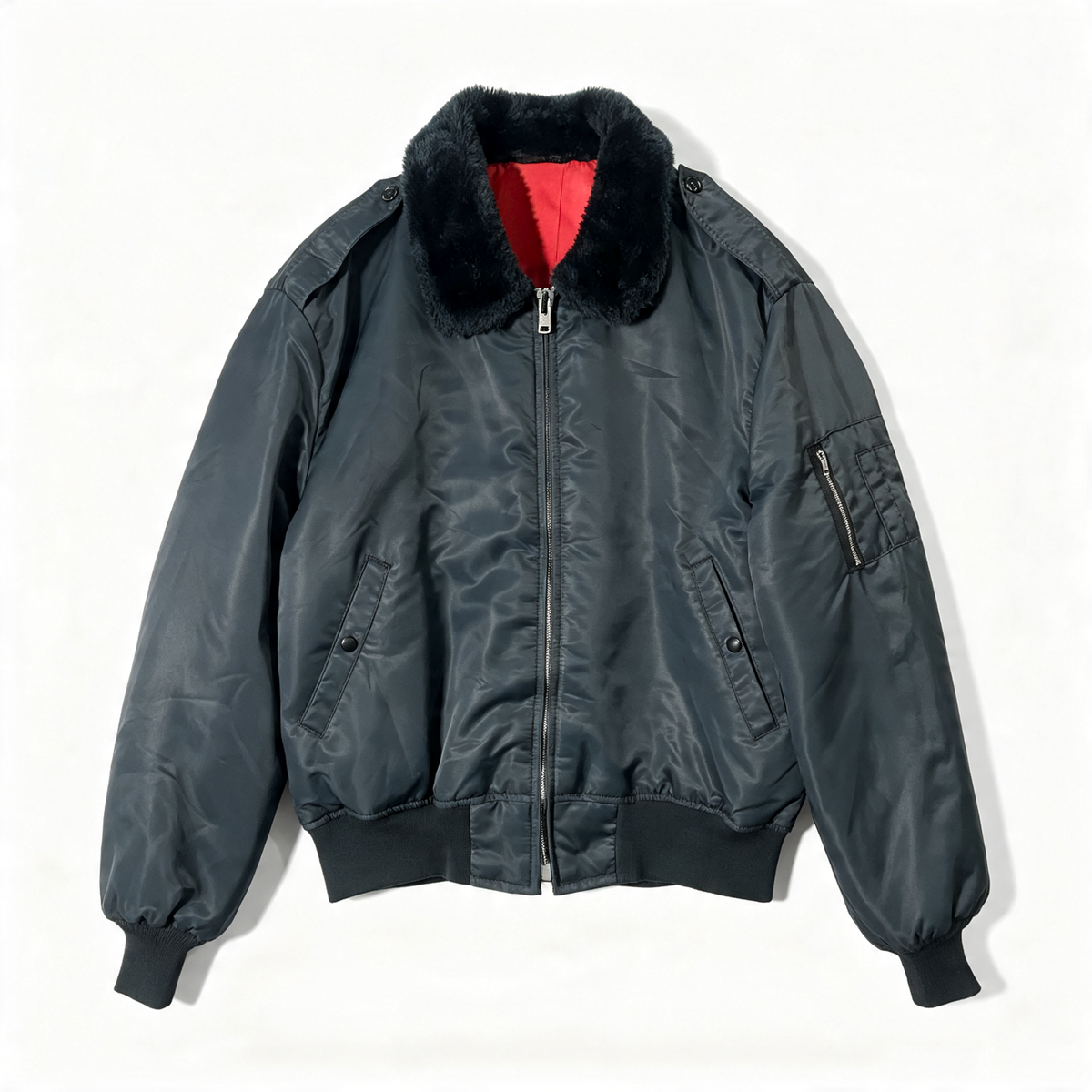 A dark gray nylon bomber jacket with a black faux-fur collar and a red lining visible inside, laid flat against a white background.
