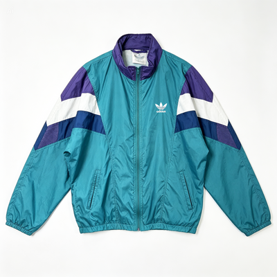 A teal Adidas windbreaker jacket with purple and white color-blocked panels on the shoulders and sleeves, featuring a white embroidered trefoil logo on the left chest, laid flat against a white background.