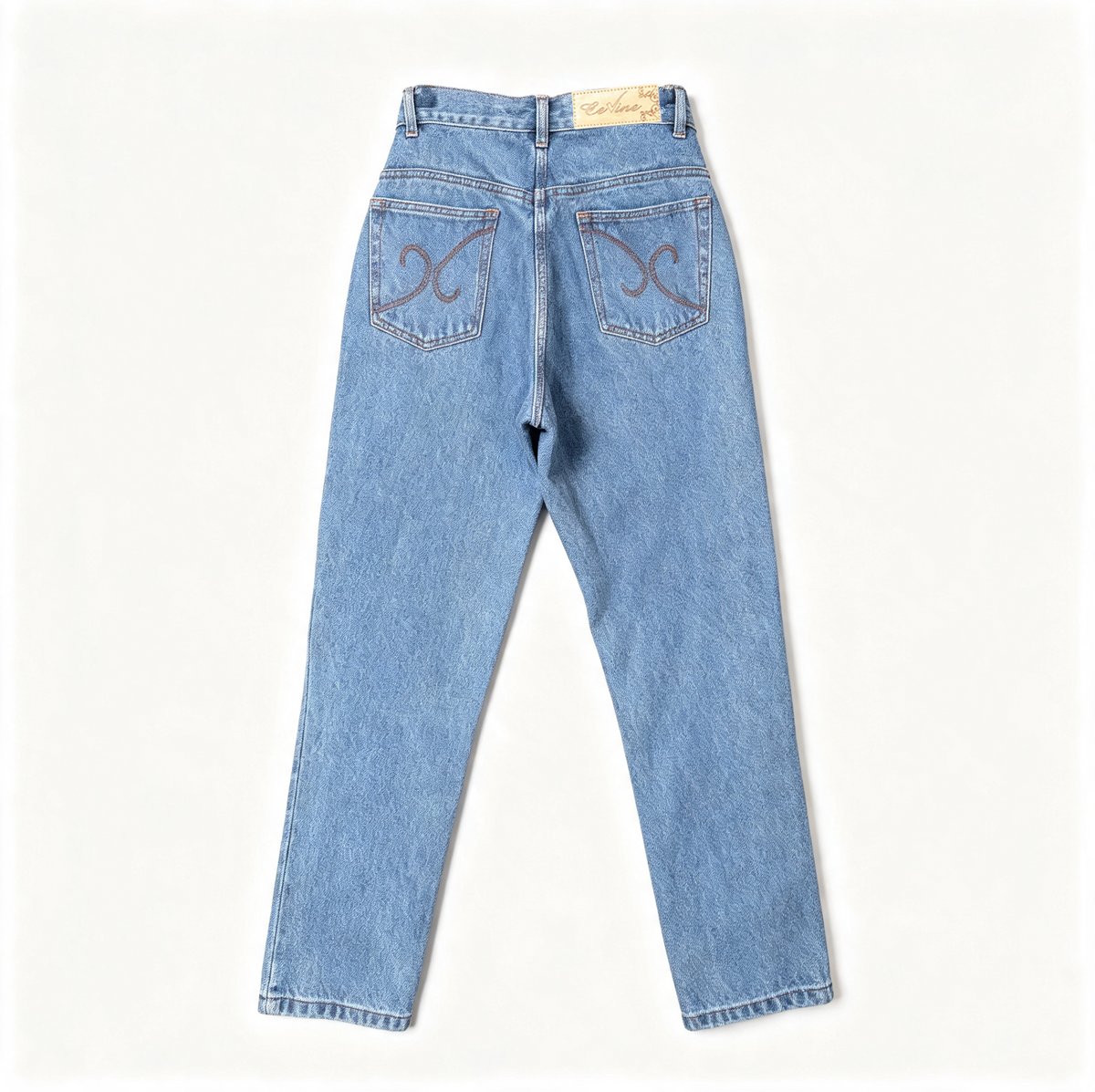 Light wash blue denim jeans shown from the back, featuring decorative embroidered swirl motifs on both back pockets and a tan brand label at the waistband, laid flat against a clean off-white background.