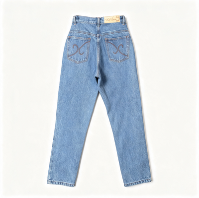 Light wash blue denim jeans shown from the back, featuring decorative embroidered swirl motifs on both back pockets and a tan brand label at the waistband, laid flat against a clean off-white background.