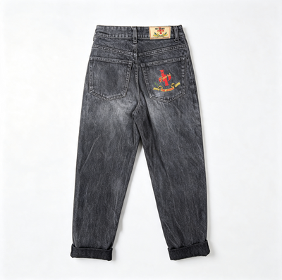 Back view of washed black denim jeans with rolled cuffs, featuring a red anchor graphic and text on the right back pocket and a small brand patch on the waistband.
