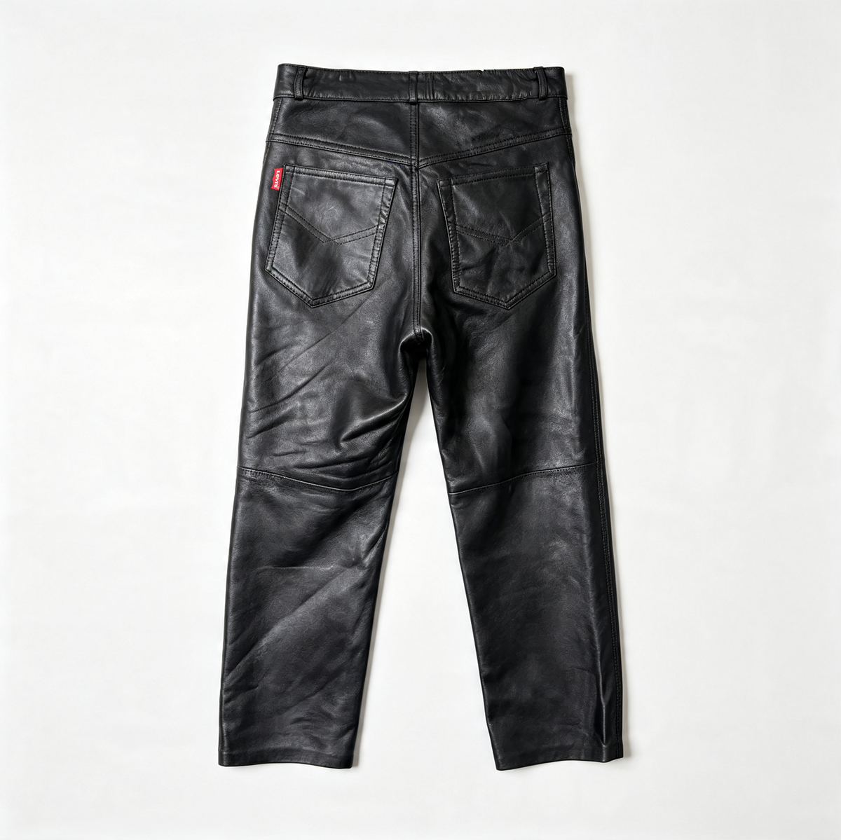 Black leather pants shown from the back, featuring a wide waistband, stitched pocket details, and a small red brand tab on the left pocket, laid flat on a white background.