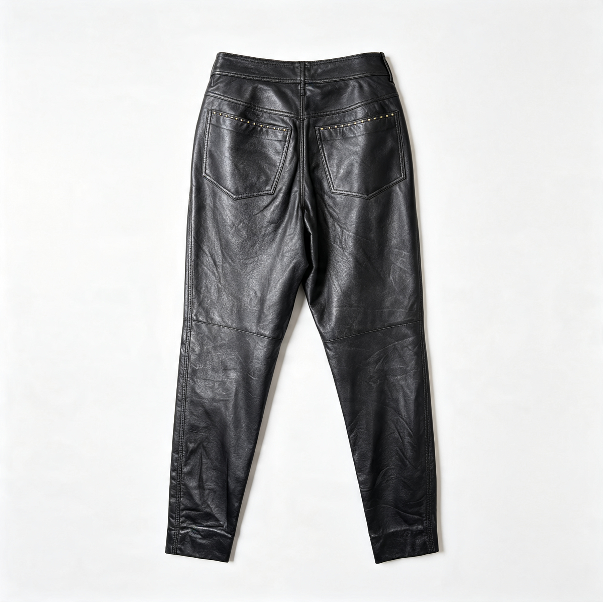 Black leather pants shown from the back, featuring two back pockets with gold-tone STUDS, laid flat on a white background.