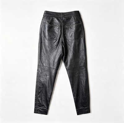 Black leather pants shown from the back, featuring two back pockets with gold-tone STUDS, laid flat on a white background.