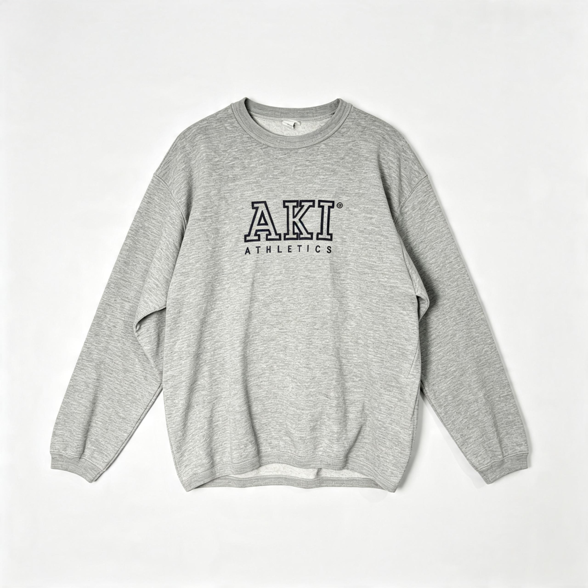 A heather gray crewneck sweatshirt with 'AKI ATHLETICS' printed in black outline block letters on the chest, laid flat against a light gray background.