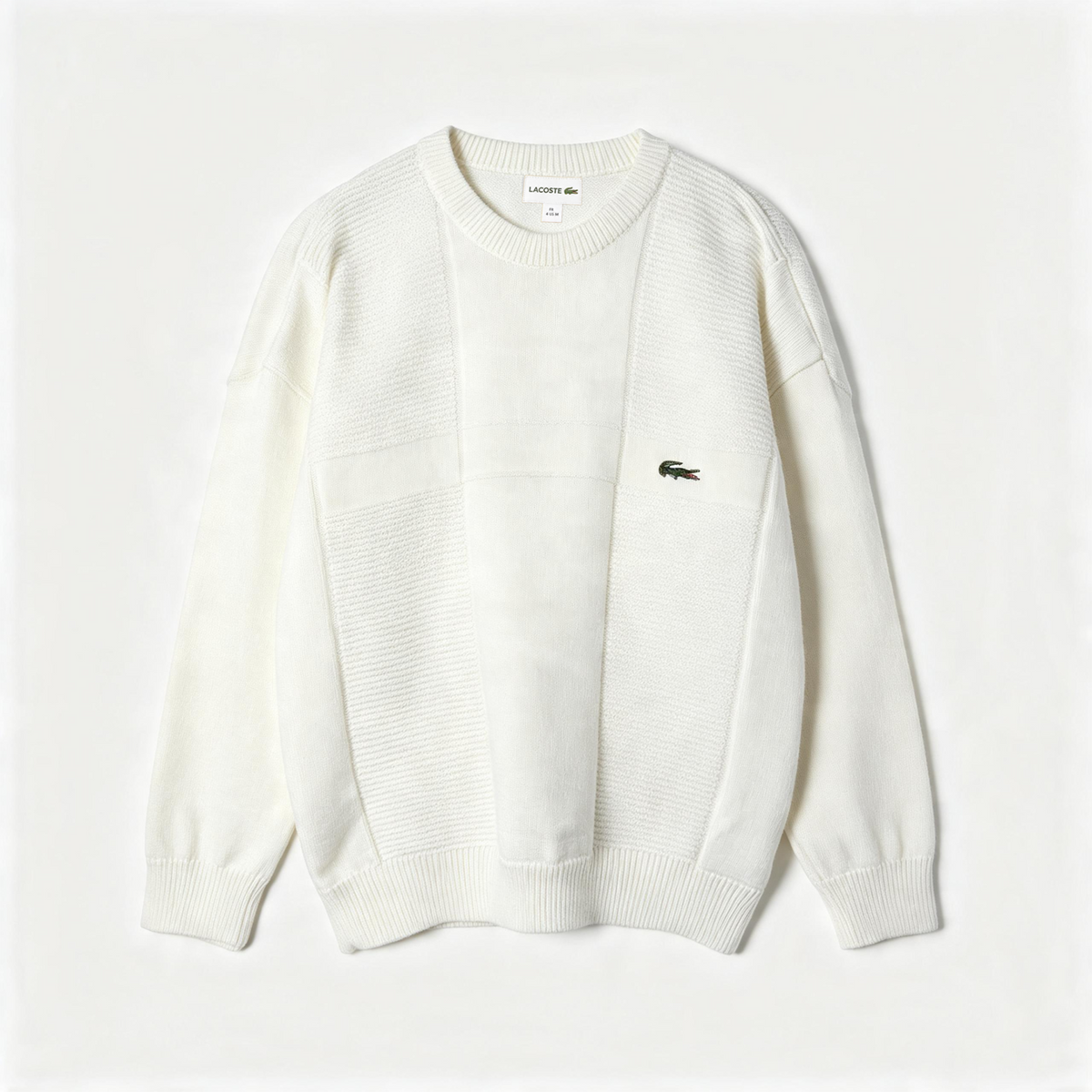 An off-white knit crewneck sweater by Lacoste, featuring a small embroidered crocodile logo on the left chest, laid flat against a light off-white background.