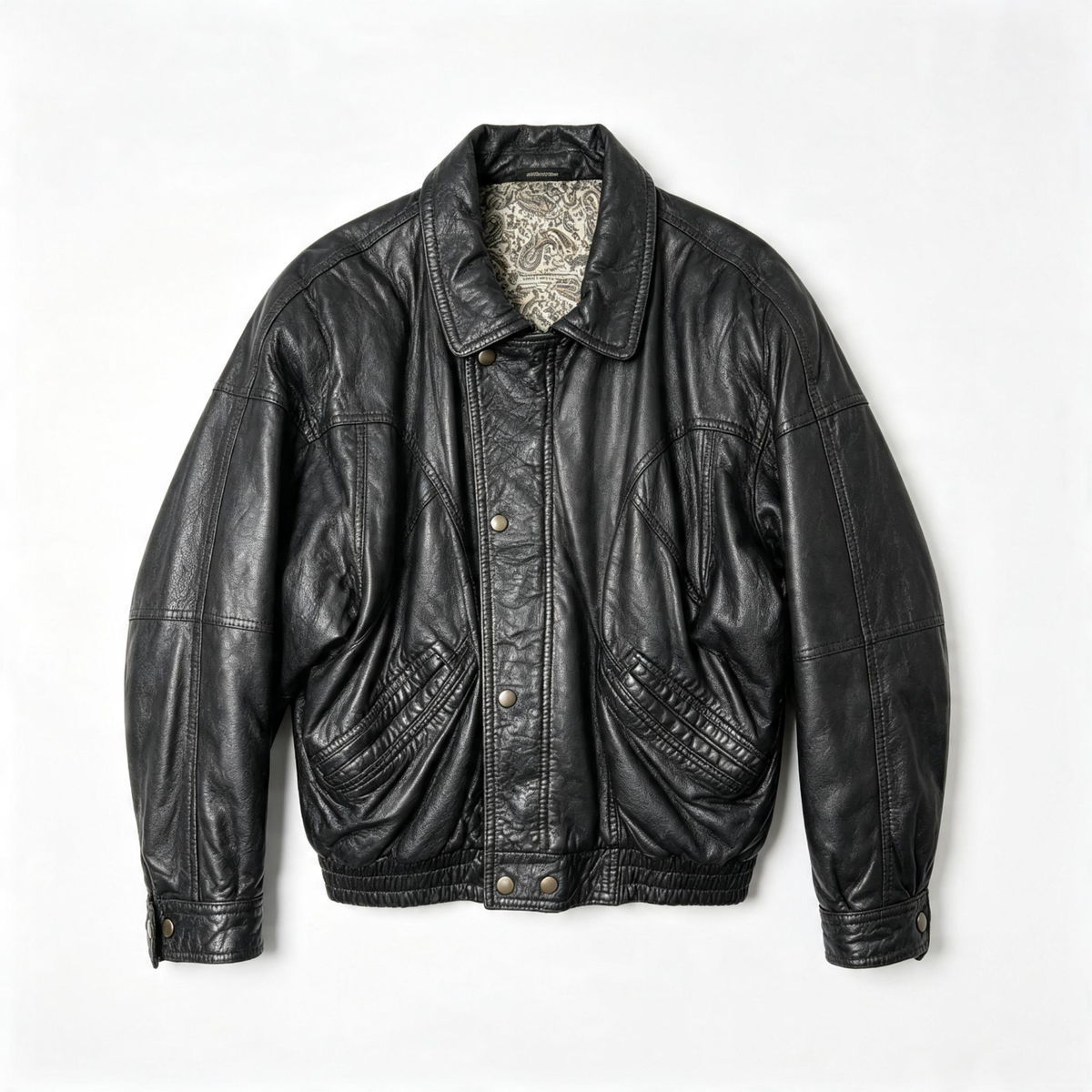 A black leather jacket with a pointed collar, button front, and quilted chest panels, laid flat against a light gray background.