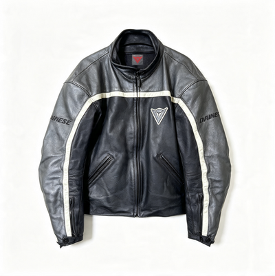 A black leather motorcycle jacket with white stripe details on the sleeves, featuring the Dainese brand name and logo, laid flat against a white background.