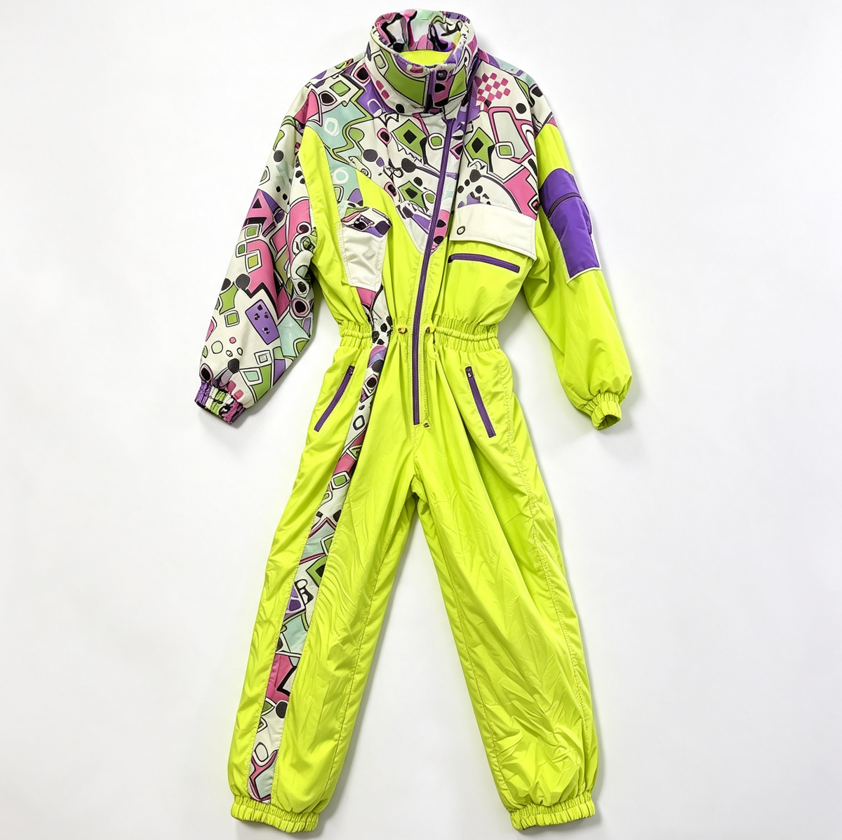 A one-piece snowsuit laid flat on a white background, featuring a bright neon yellow-green base with multicolor geometric patterns on the upper chest, shoulders, and sleeves, and purple zipper accents.