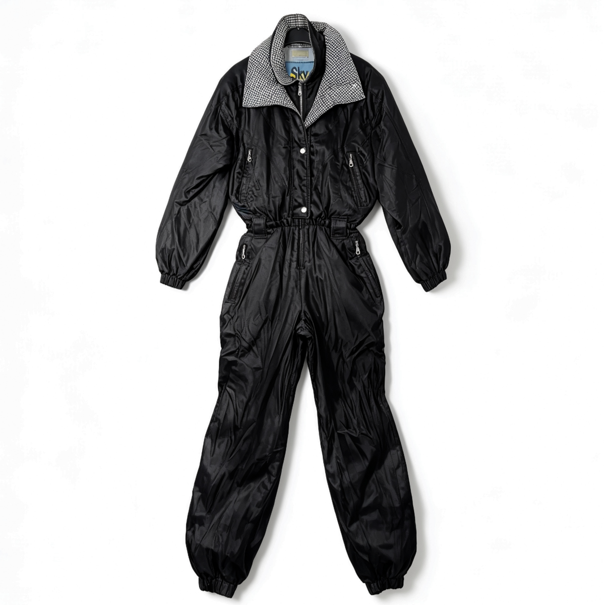 A black nylon jumpsuit with a gingham patterned collar, laid flat against a white background.
