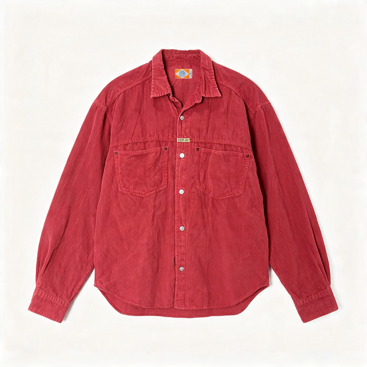 A red corduroy button-up shirt with two chest pockets and a small gold-tone brand plaque, laid flat against a light cream background.