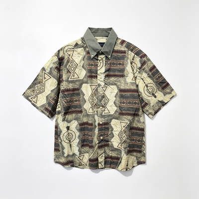 A short-sleeve button-up shirt with a geometric tribal-inspired pattern in beige, brown, and gray, featuring a solid gray collar, laid flat against a white background.