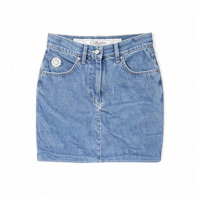 A light blue denim mini skirt with a button fly, belt loops, and a decorative silver-tone flower embellishment on the left pocket, shown flat on a white background.