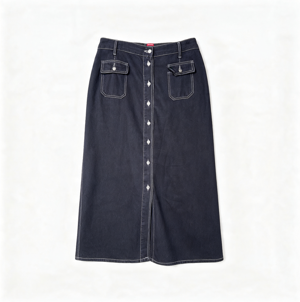 A dark navy blue denim skirt with white contrast stitching, featuring a button-down front, two flap pockets with snap closures, and a button waistband, shown flat on a white background.