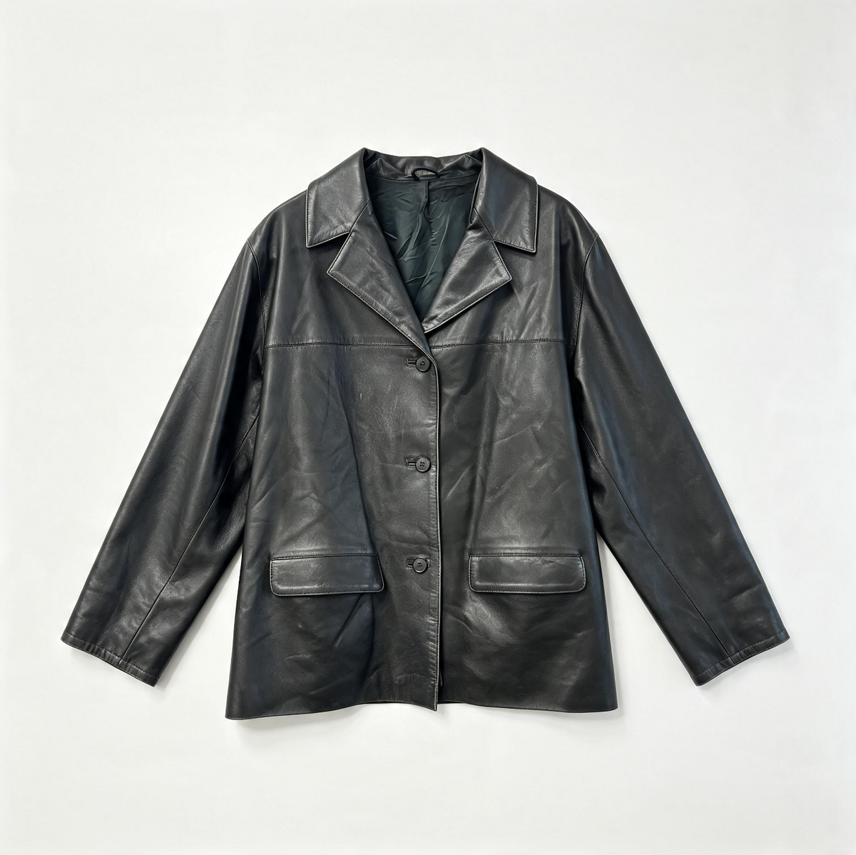 A black leather jacket with a notched lapel collar, three-button front closure, and two front flap pockets, laid flat against a light gray background.